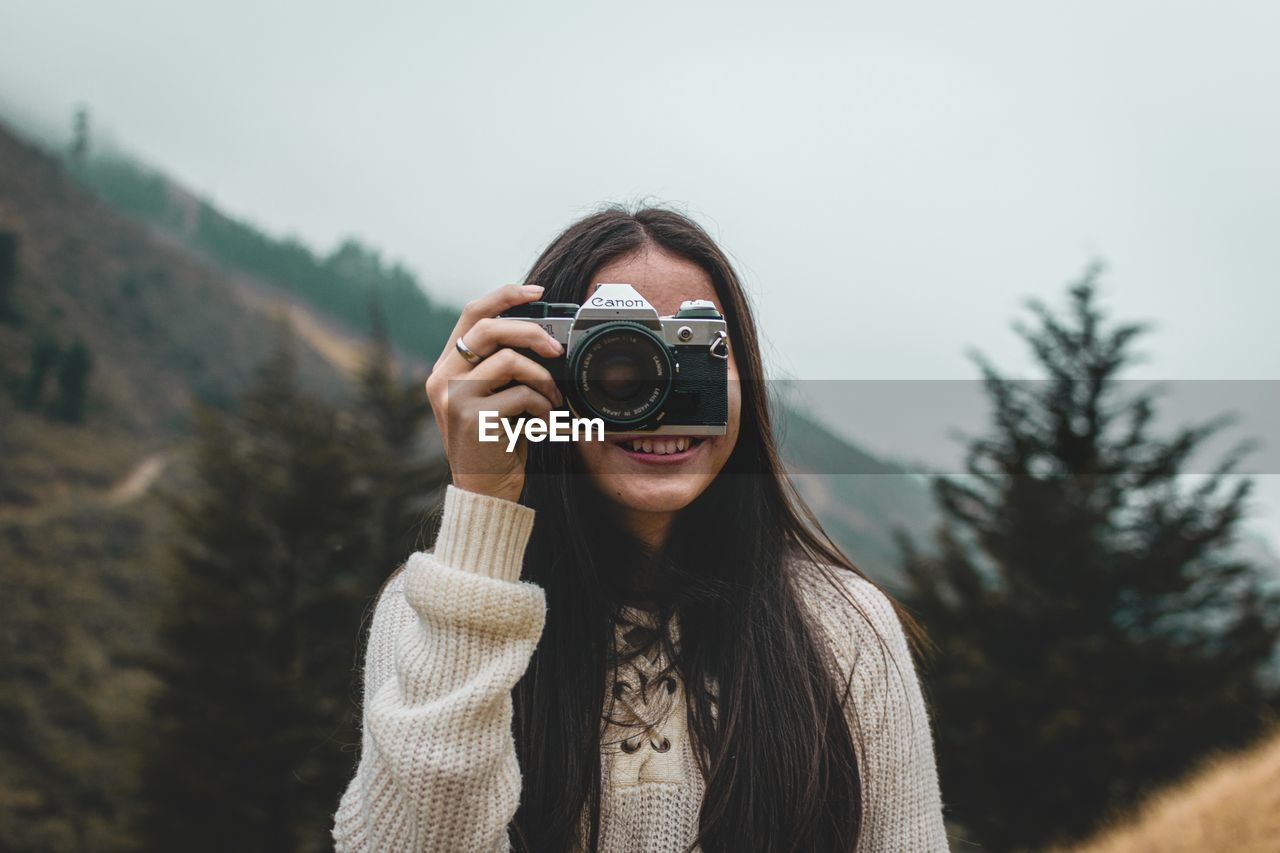 PORTRAIT OF YOUNG WOMAN PHOTOGRAPHING WITH CAMERA