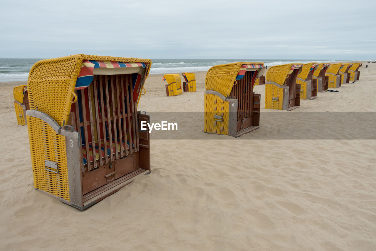 HOODED BEACH CHAIRS ON SAND AGAINST SKY