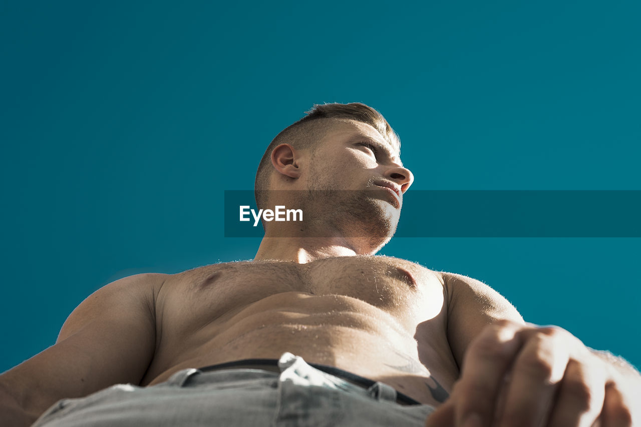 Low angle view of shirtless man standing against clear blue sky
