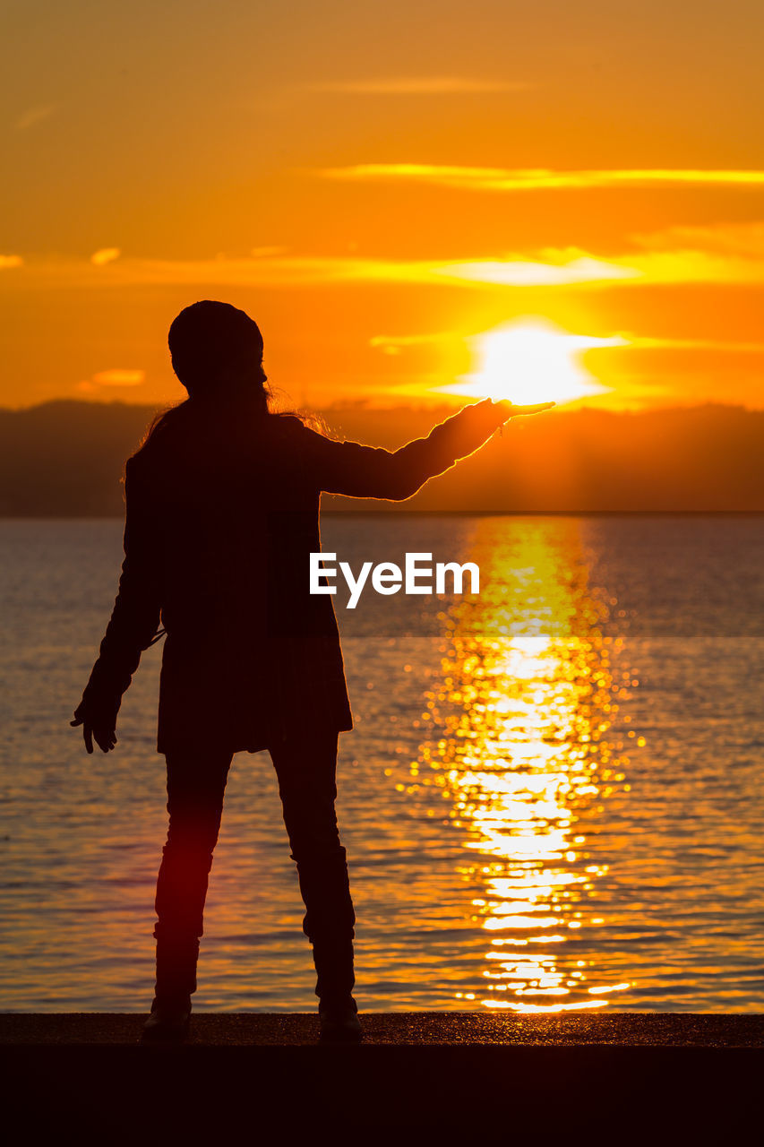 Silhouette woman standing on beach against orange sky