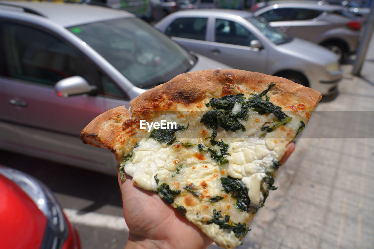 CLOSE-UP OF HAND HOLDING PIZZA ON CAR