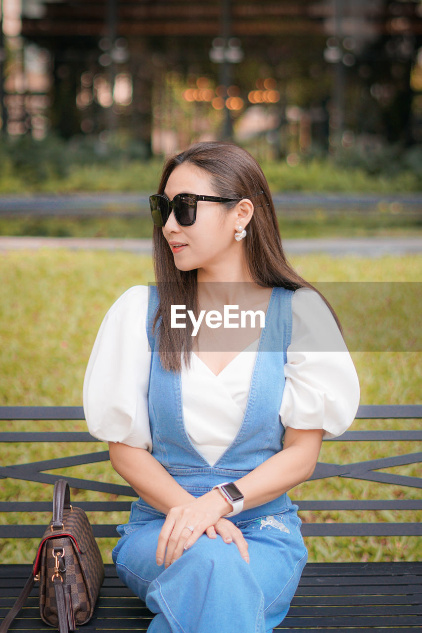 Beautiful woman wearing sunglasses sitting on bench at park