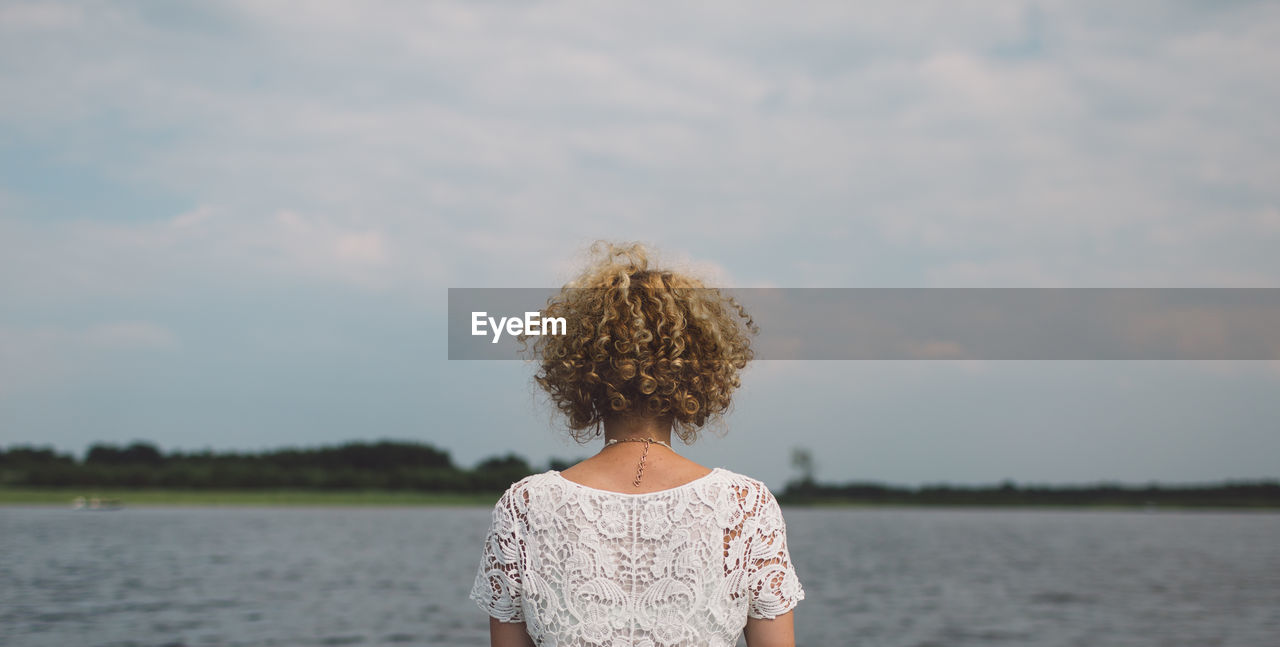 Rear view of woman standing by lake against sky