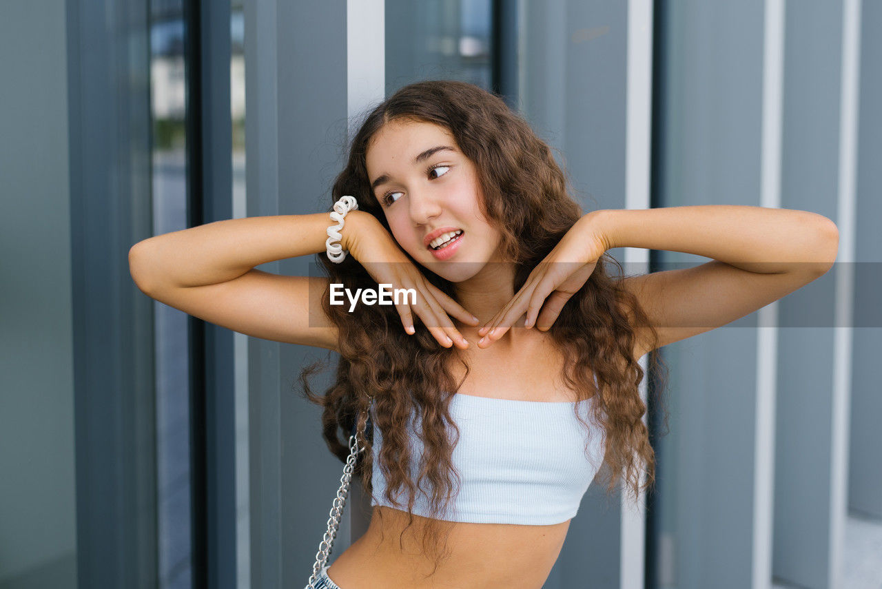 A fashionable teenager playfully posing near a modern building with large glass windows