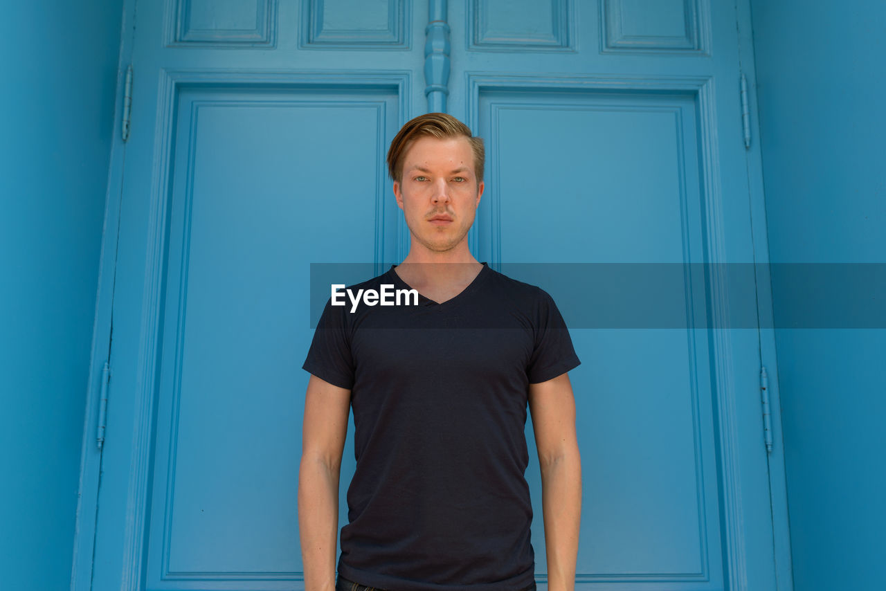 Portrait of man standing against blue door