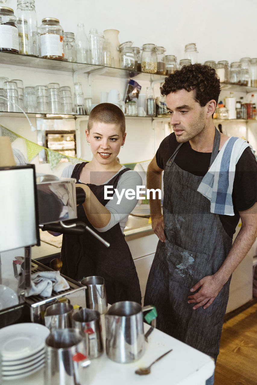 Female and male owners learning to use coffee maker at cafe