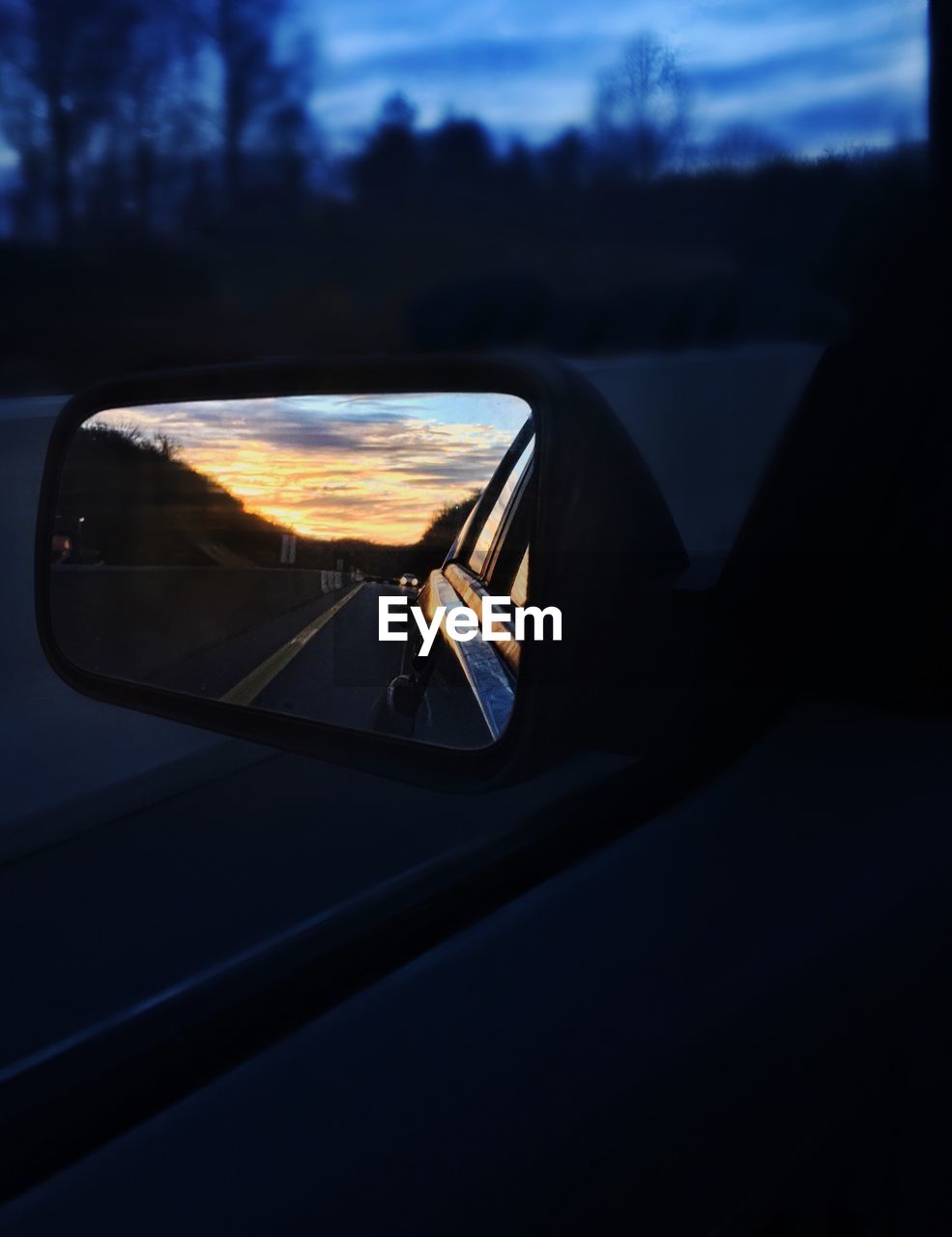 Road reflecting on side-view mirror of car during sunset