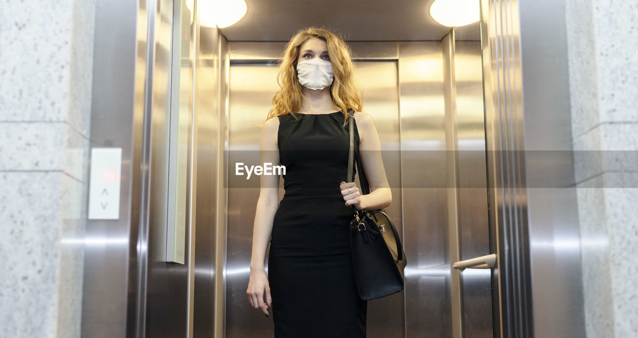 Young woman wearing mask standing in elevator