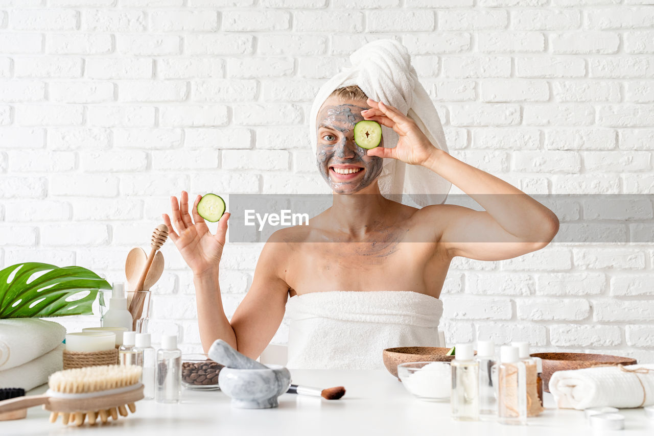 Young woman wearing white towels applying spa facial mask on her face with a cosmetic brush