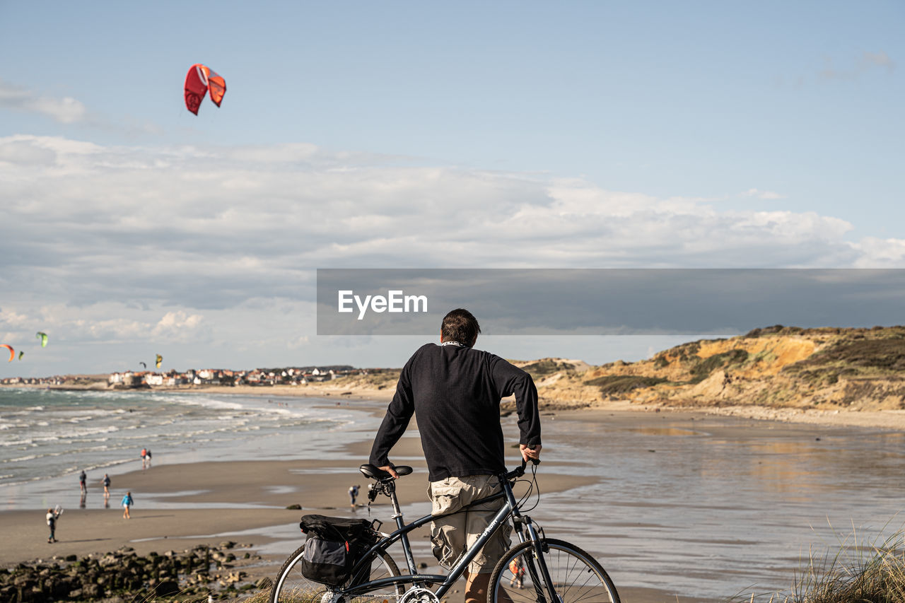 MAN WITH BICYCLE AT BEACH AGAINST SKY