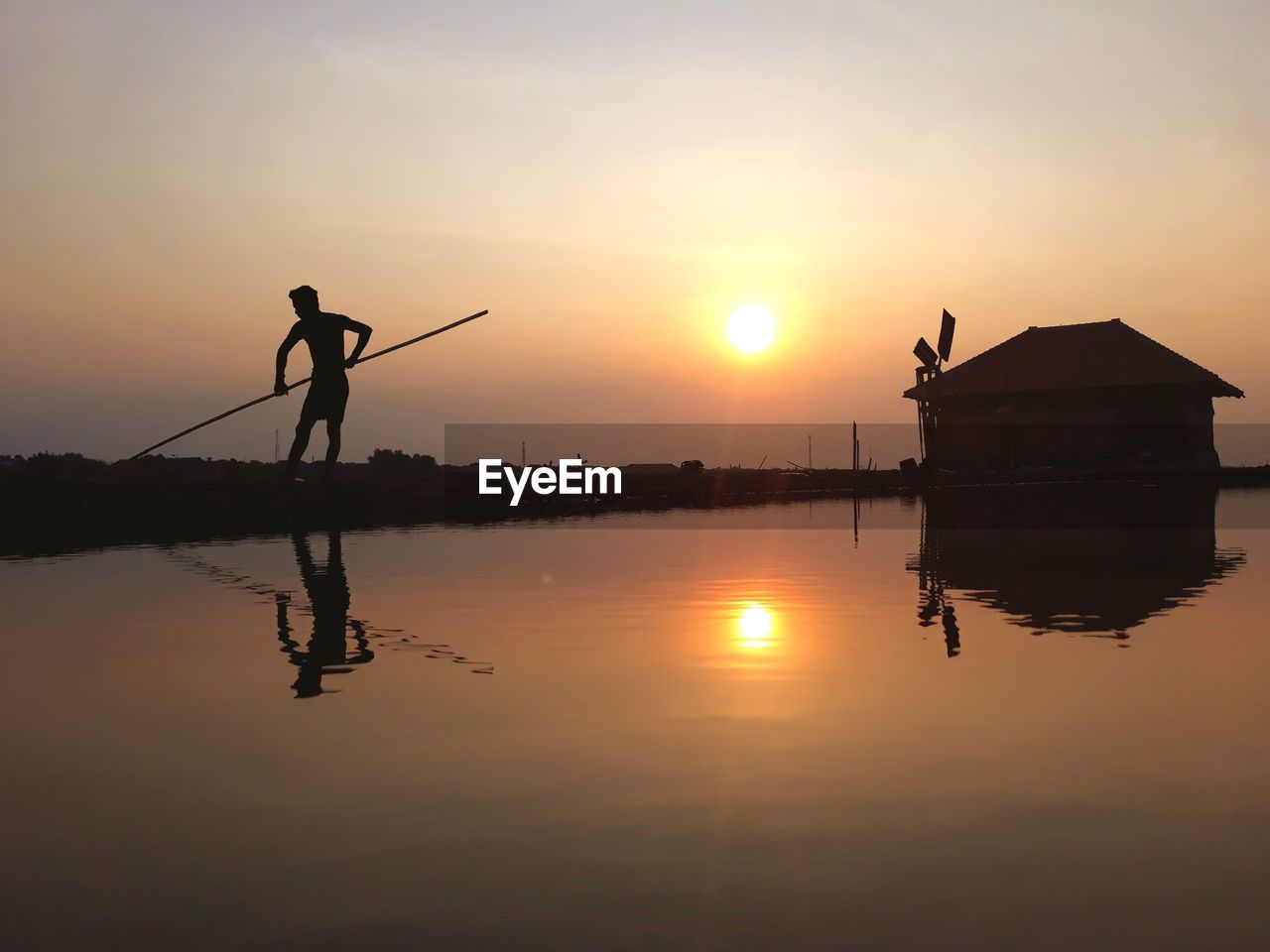 Silhouette man by lake against sky during sunset