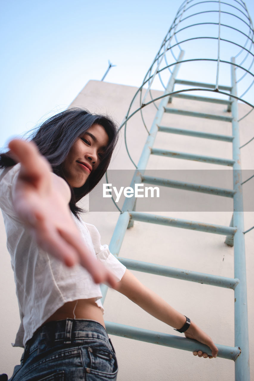 Low angle portrait of woman climbing on ladder