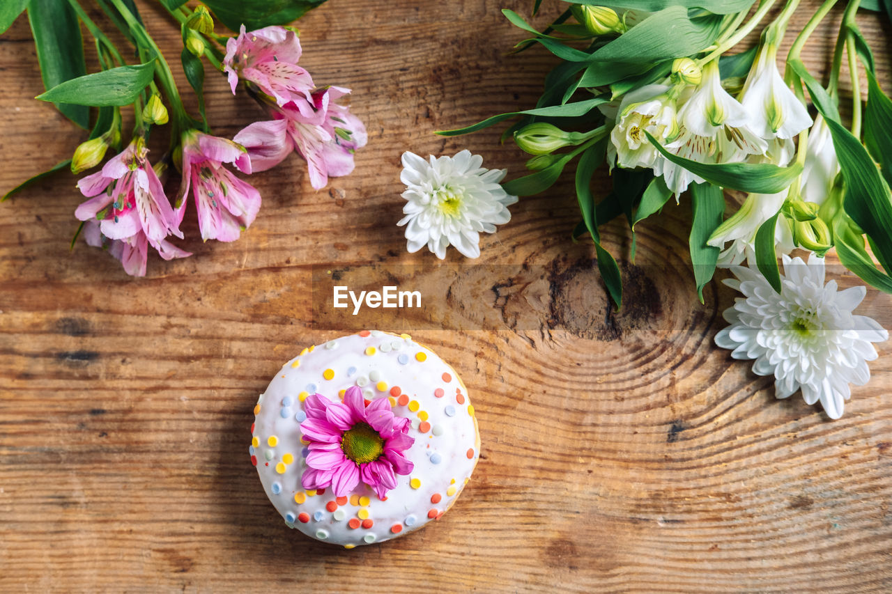 Chamomile bud on top of a donut on a wooden background with a bouquet of alstroemerias. 	
