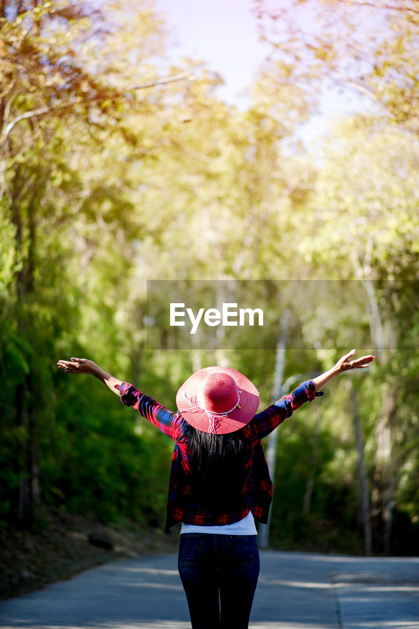 Rear view of woman with arms outstretched standing against trees