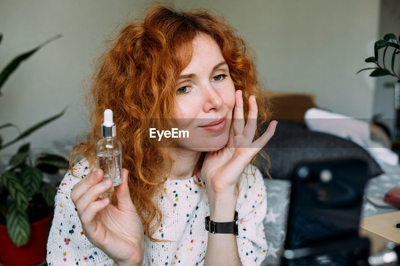 Young curly redhead female blogger filming daily tutorial for social media