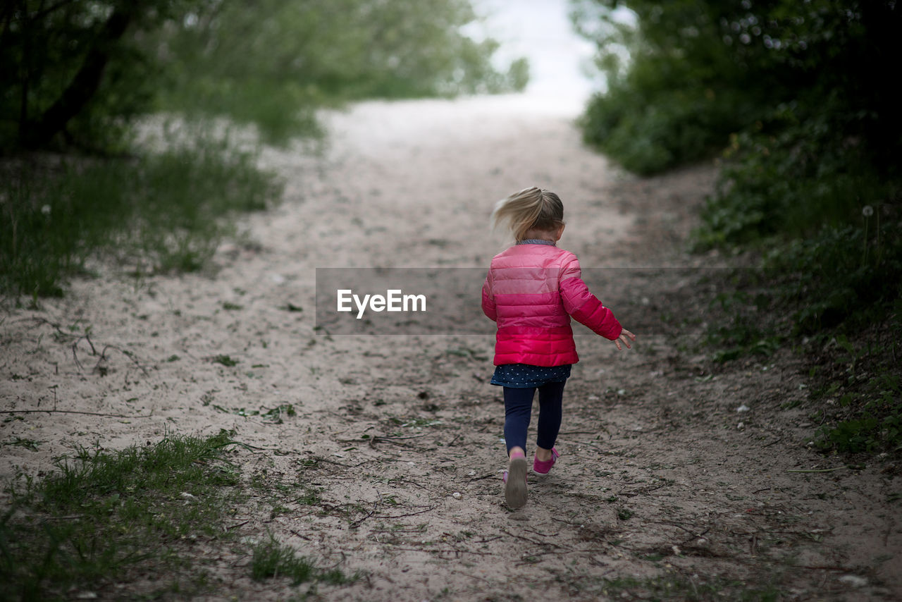Rear view of girl walking on dirt road