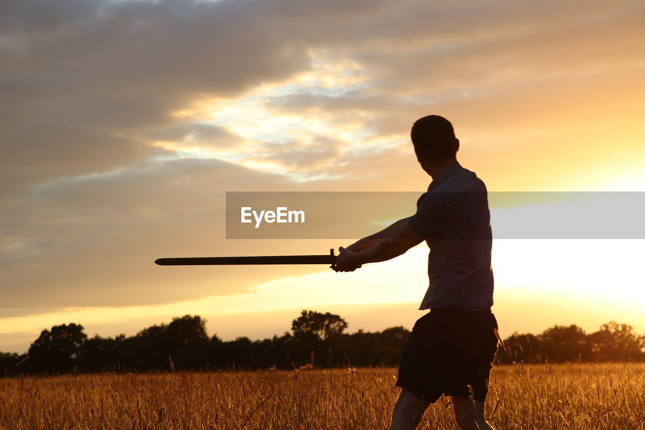 MAN STANDING ON FIELD AT SUNSET