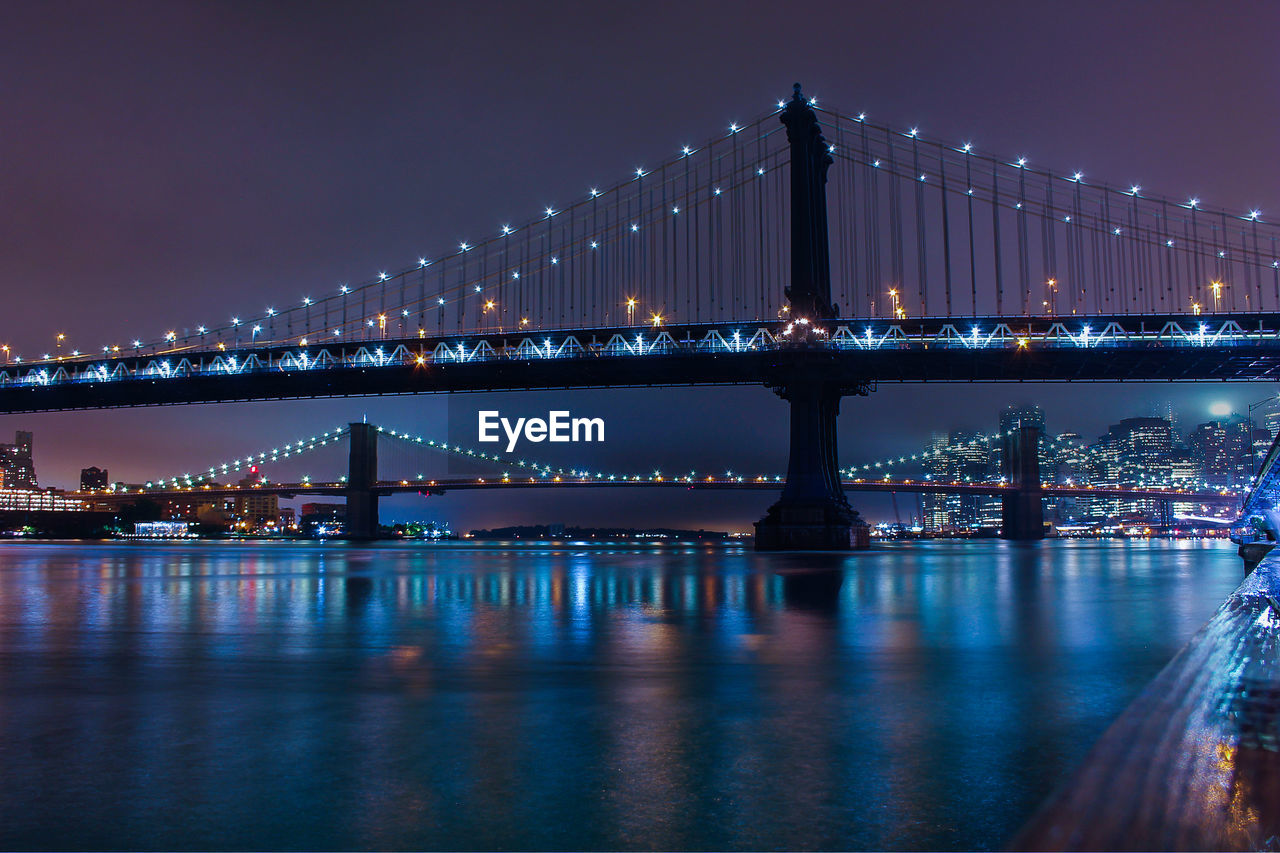 Manhattan bridge over river against sky at night