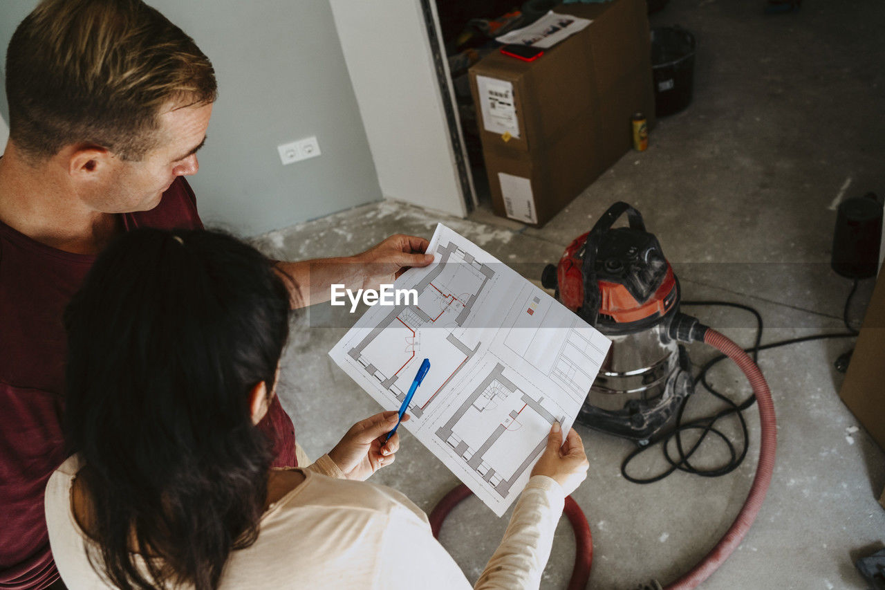 High angle view of couple discussing over blueprint while renovating home