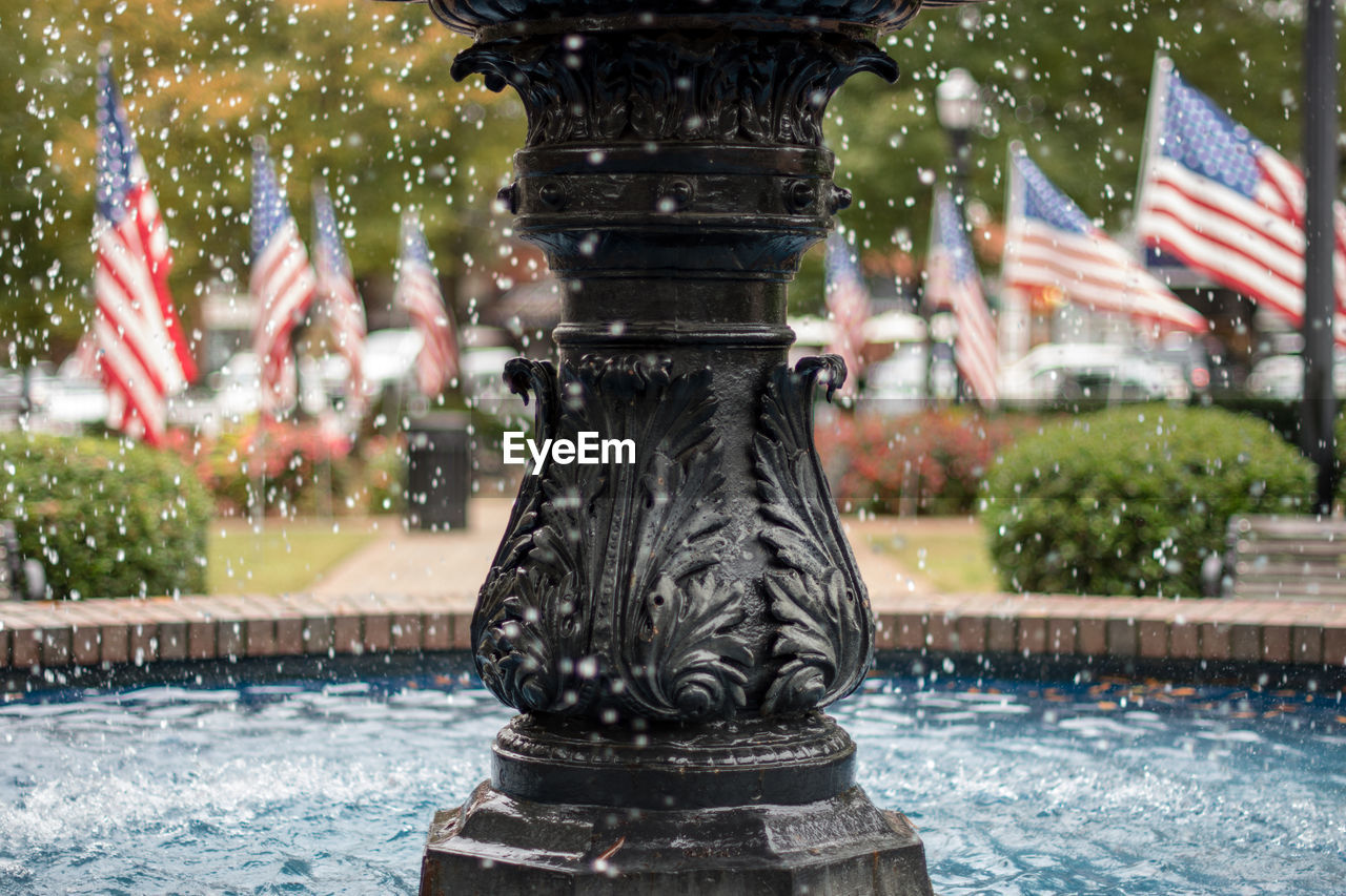 Close-up of fountain against american flags in park