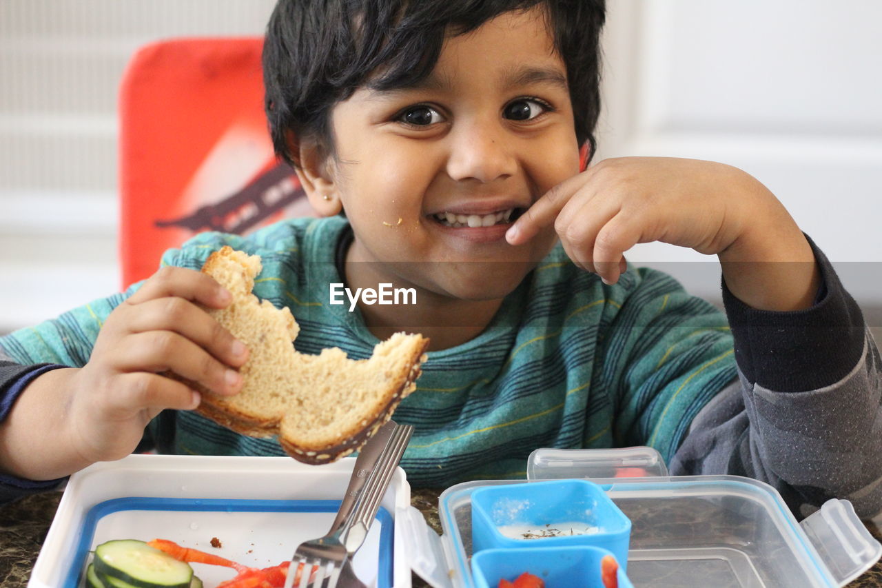 Portrait of smiling boy eating while sitting at table