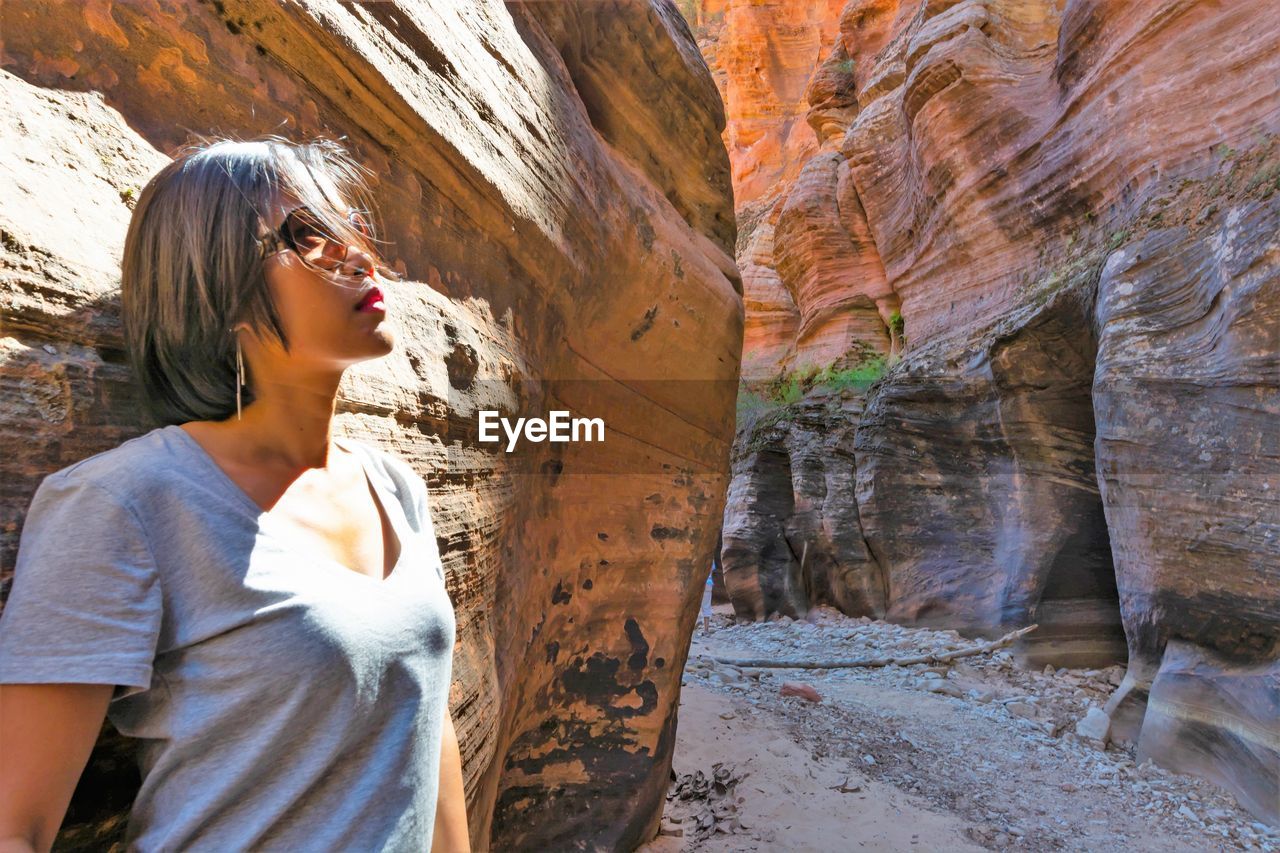 Woman wearing sunglasses standing by rock formation