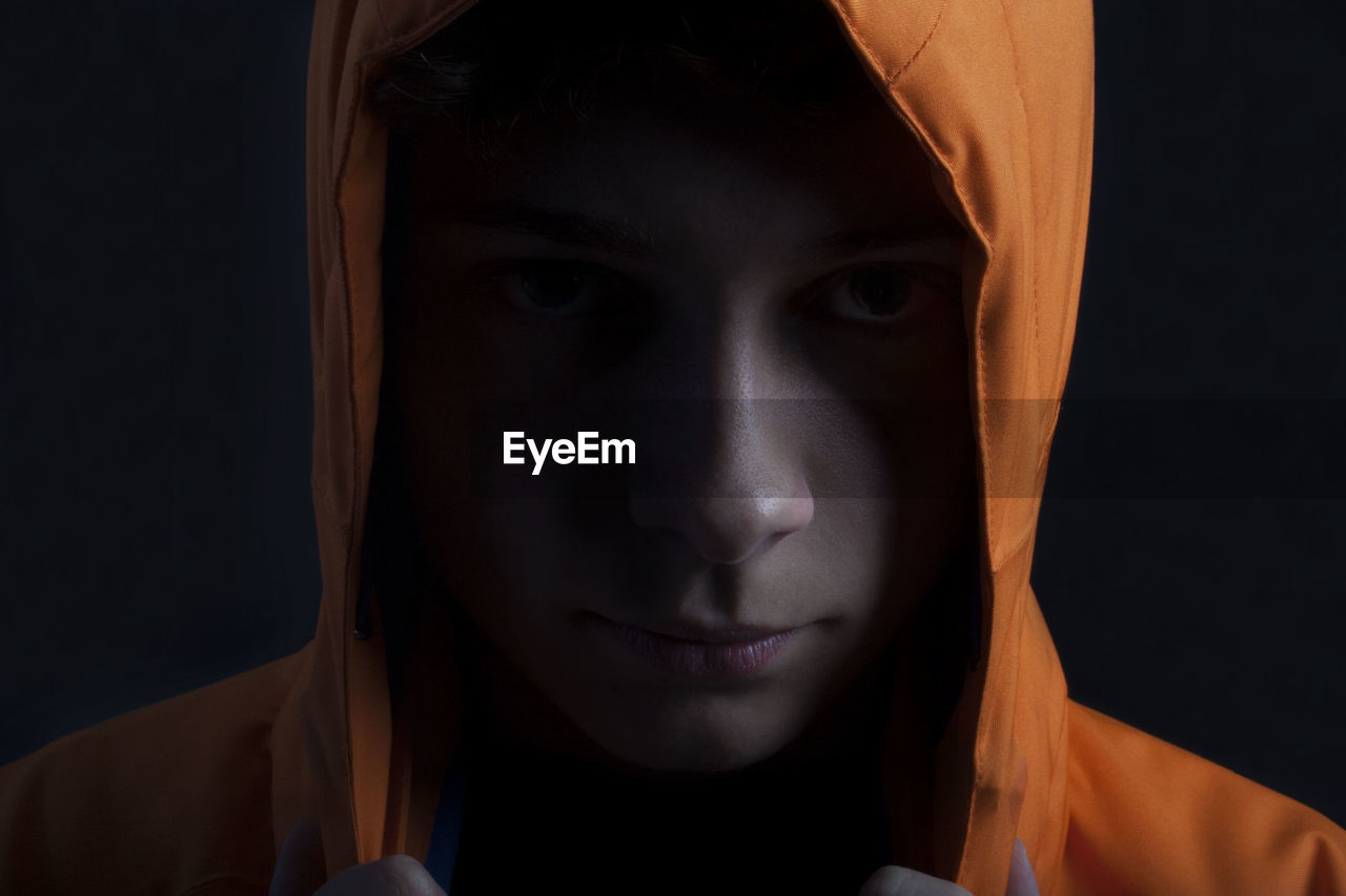 Close-up portrait of young woman in hooded shirt against black background