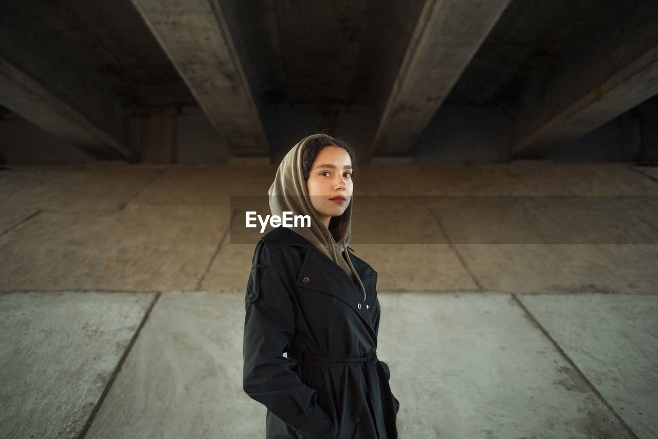 PORTRAIT OF YOUNG WOMAN STANDING IN CONCRETE