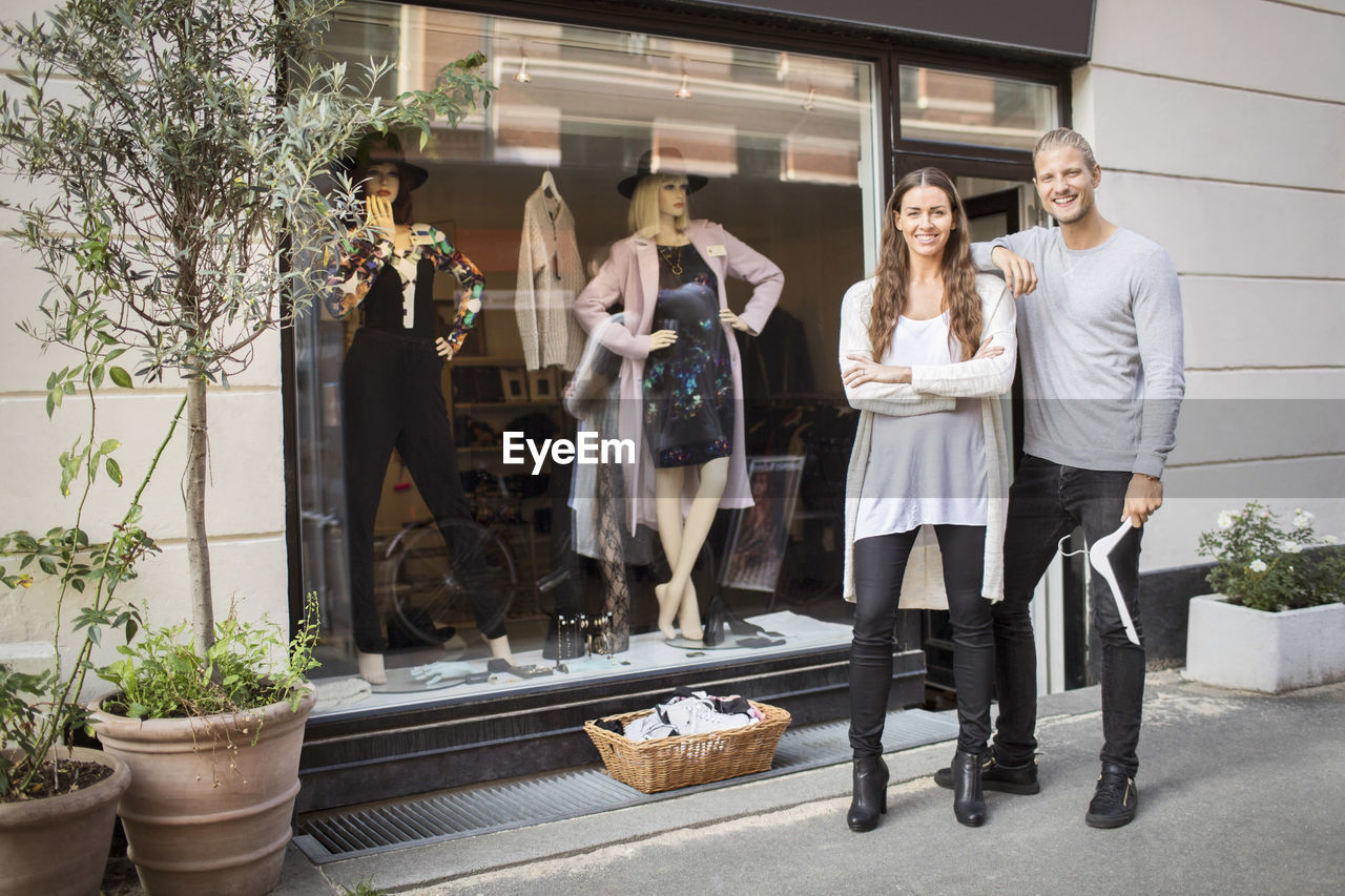 Portrait of smiling owner with female worker standing in front of clothing store