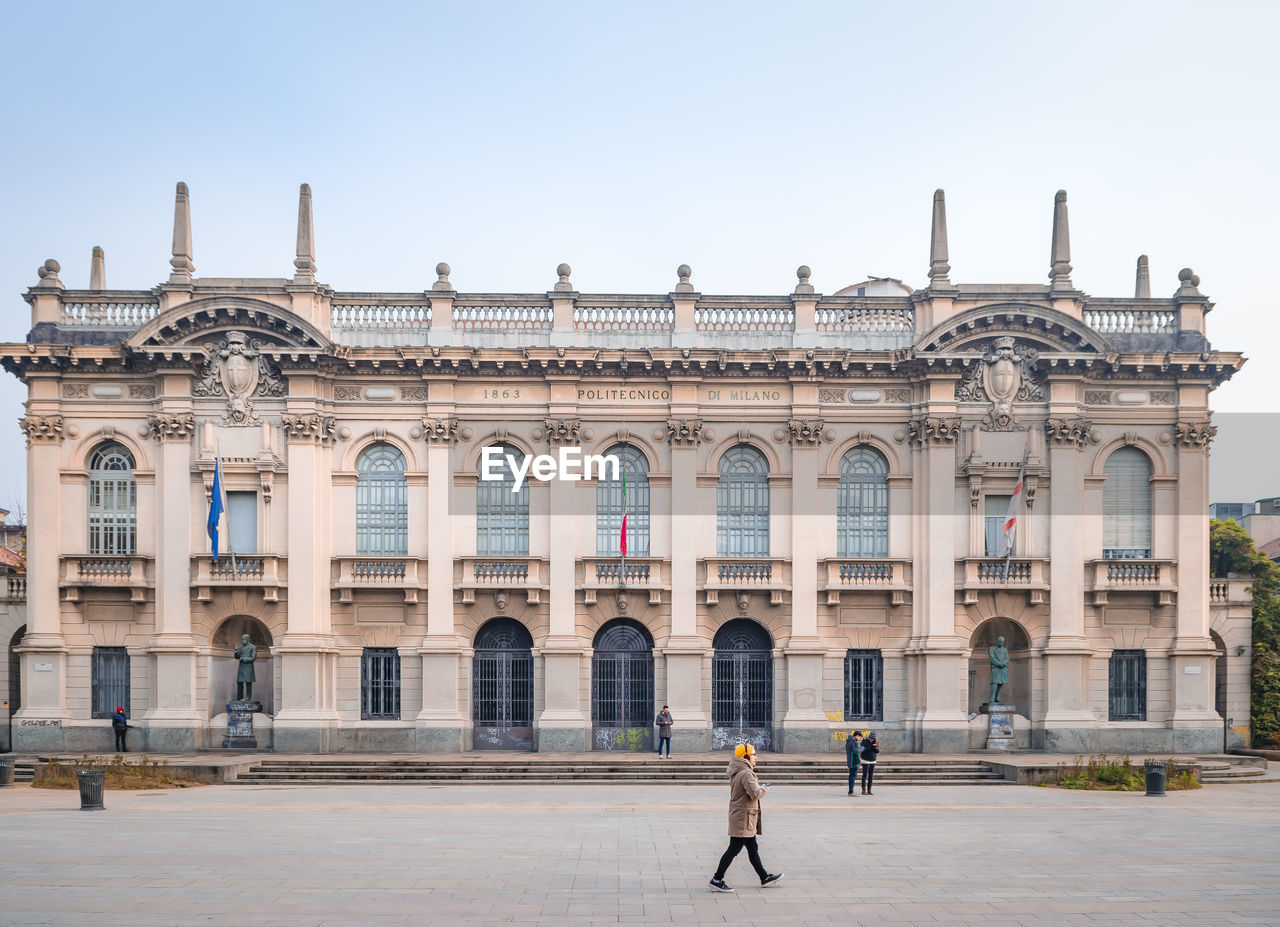 People walking in front of historical building against sky