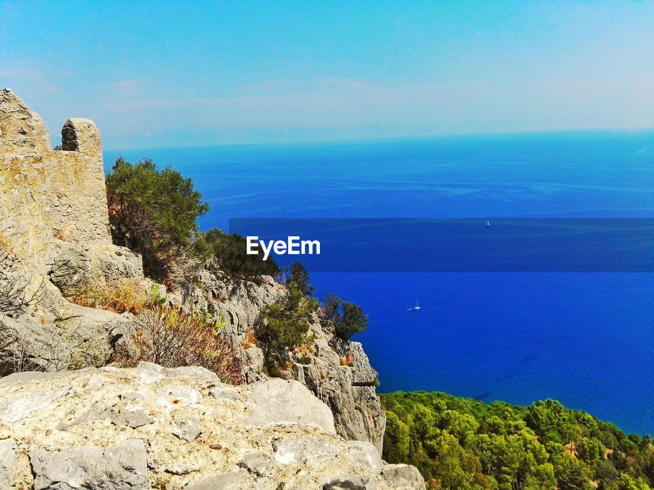 ROCKS BY SEA AGAINST BLUE SKY