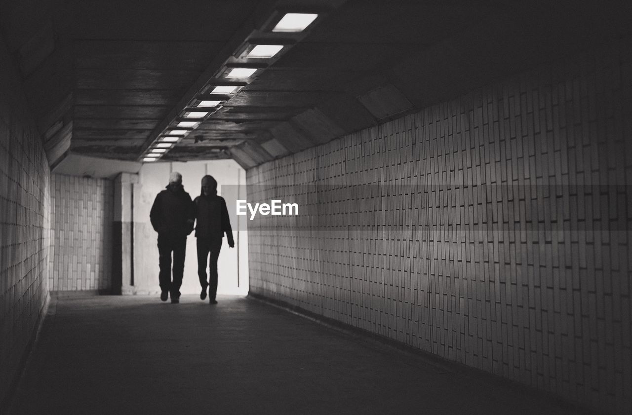 Silhouette view of two strangers walking in a tunnel
