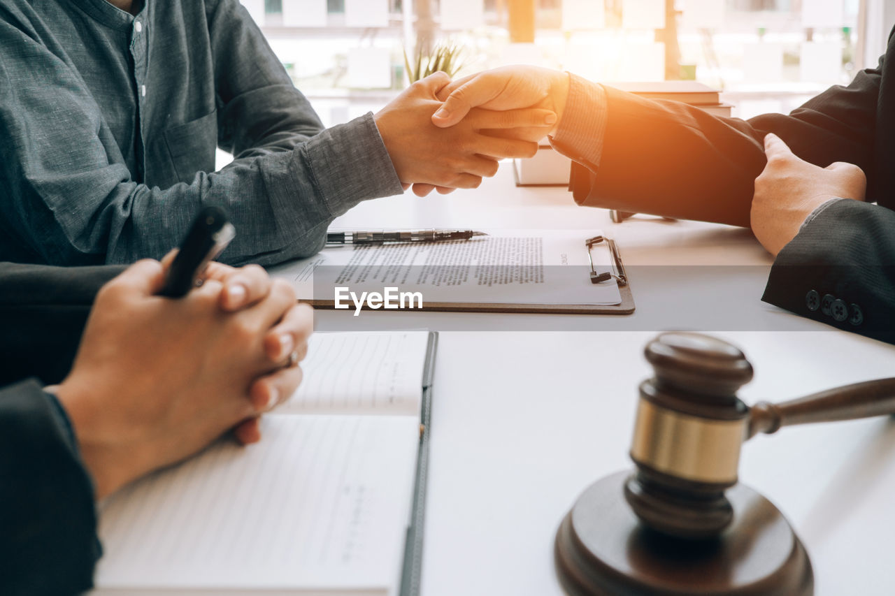 Midsection of lawyer shaking hands with colleague while sitting at desk