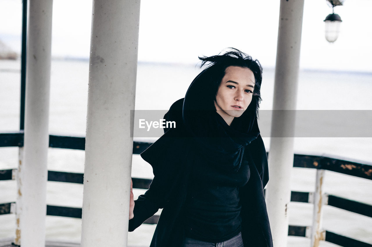 Portrait of beautiful young woman standing in gazebo against sea