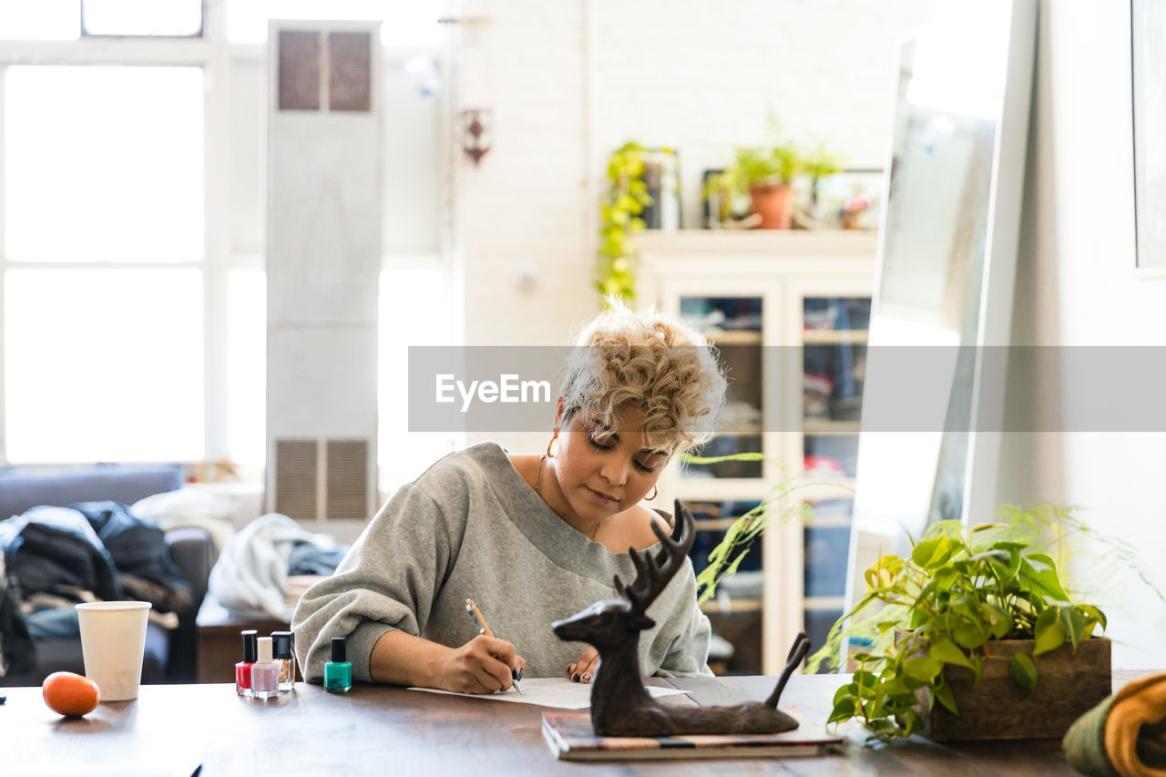 Mid adult woman writing at table while sitting in living room