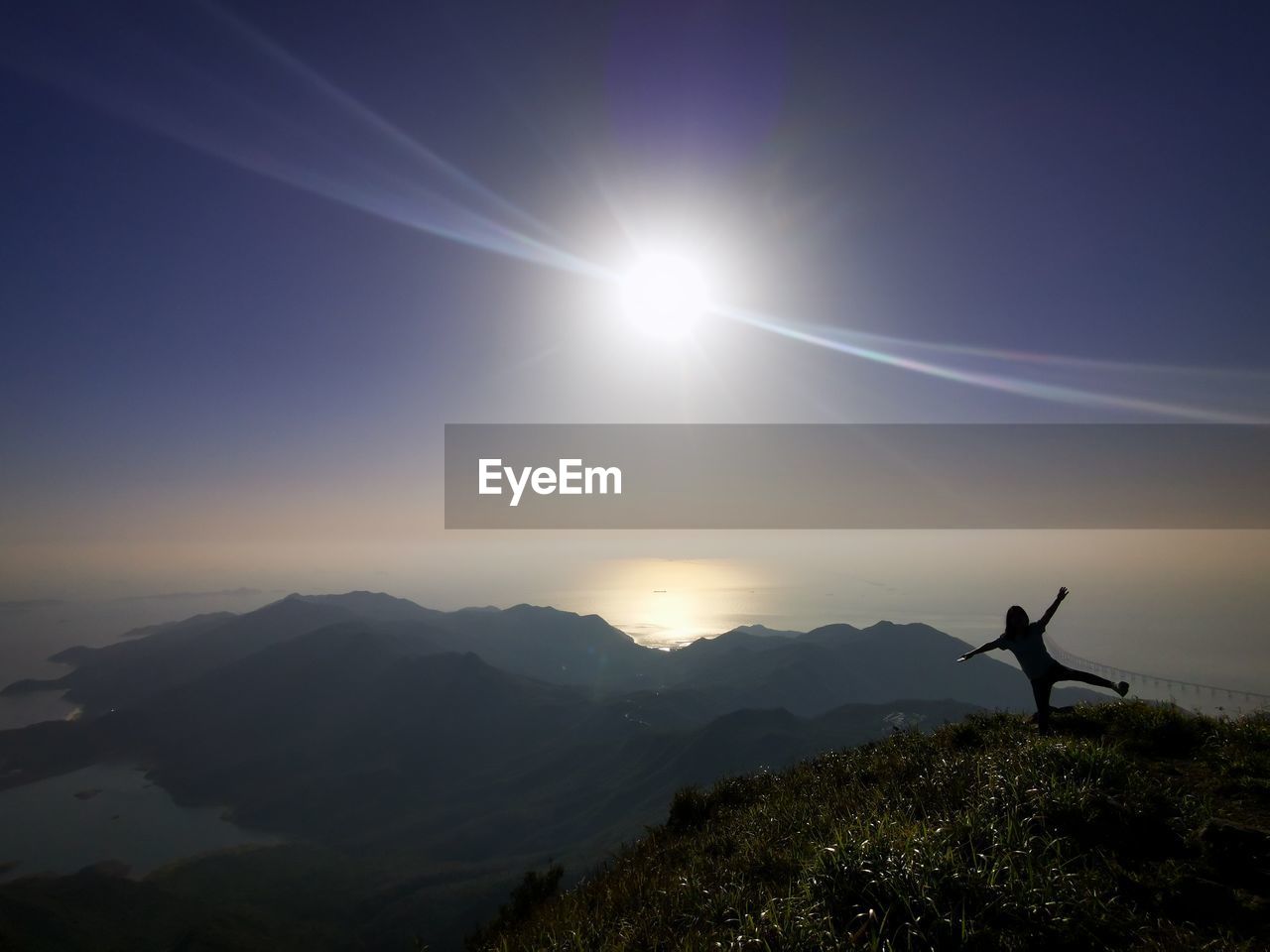 sky, mountain, environment, silhouette, nature, scenics - nature, beauty in nature, one person, sun, landscape, horizon, sunlight, arm, tranquility, sunbeam, sunrise, tranquil scene, mountain range, leisure activity, back lit, cloud, adult, dawn, idyllic, lens flare, limb, adventure, land, outdoors, standing, arms raised, non-urban scene, morning, success, travel, light, spirituality, human limb, activity, lifestyles, religion, holiday, vacation, blue, men, arms outstretched, trip, sports, aspirations, darkness