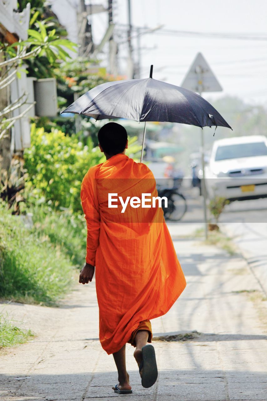 Rear view of monk walking on road in city