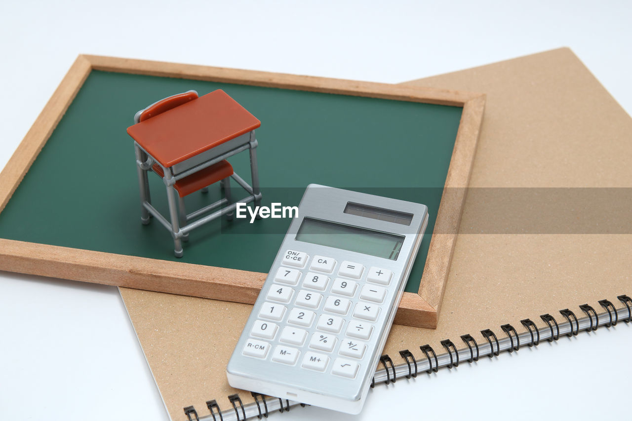 Close-up of small desk by book and chalkboard over white background