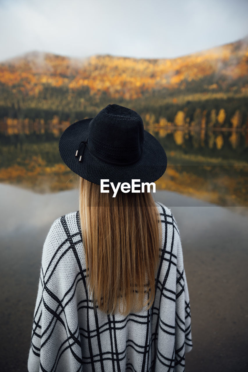 Young blonde woman wearing poncho and hat near the autumn forest. wanderlust,travel concept.