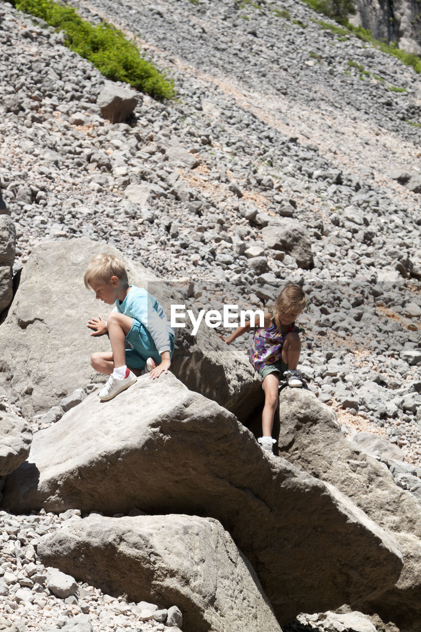 Cute sibling sitting on rock outdoors