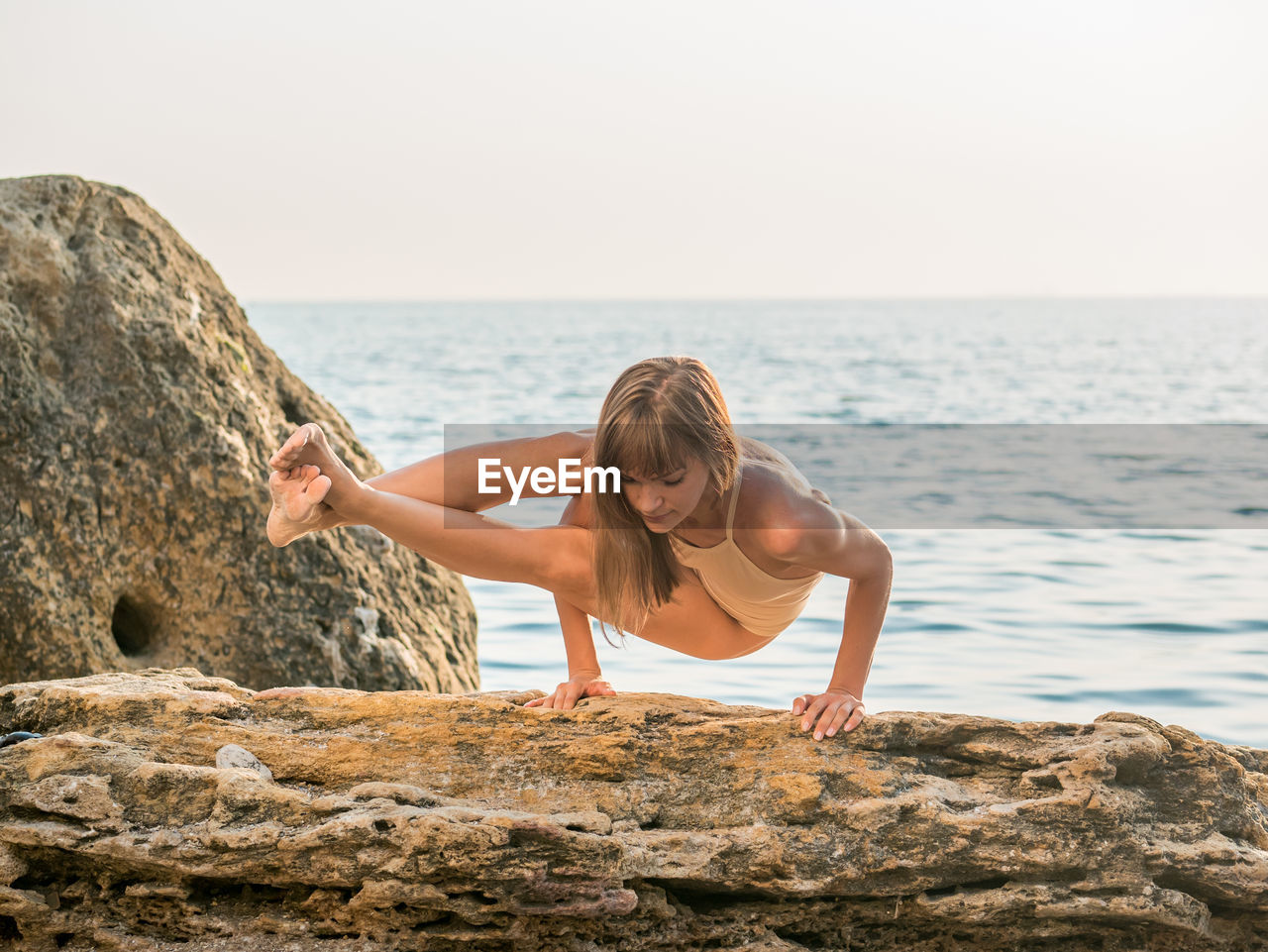 Full length of young woman practicing yoga on rock by sea