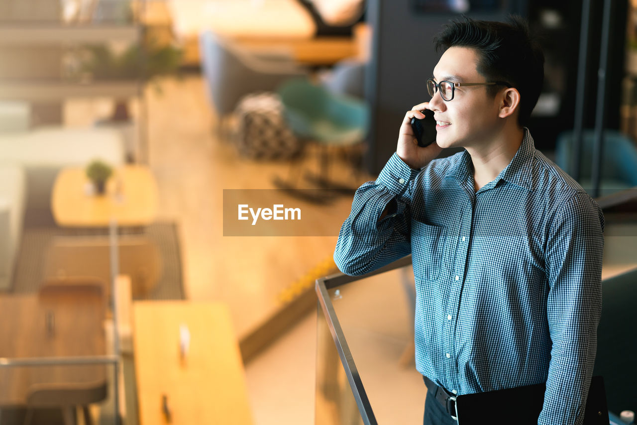 YOUNG MAN USING MOBILE PHONE WHILE STANDING IN THE CAMERA