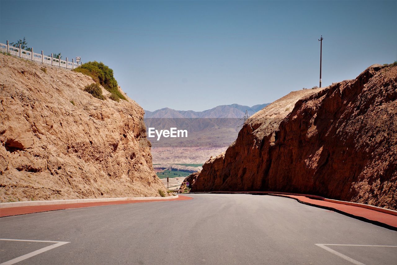 Road leading towards mountains against clear sky