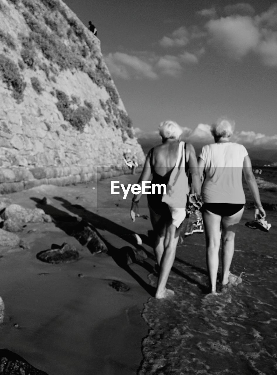 Full length rear view senior female friends walking at beach