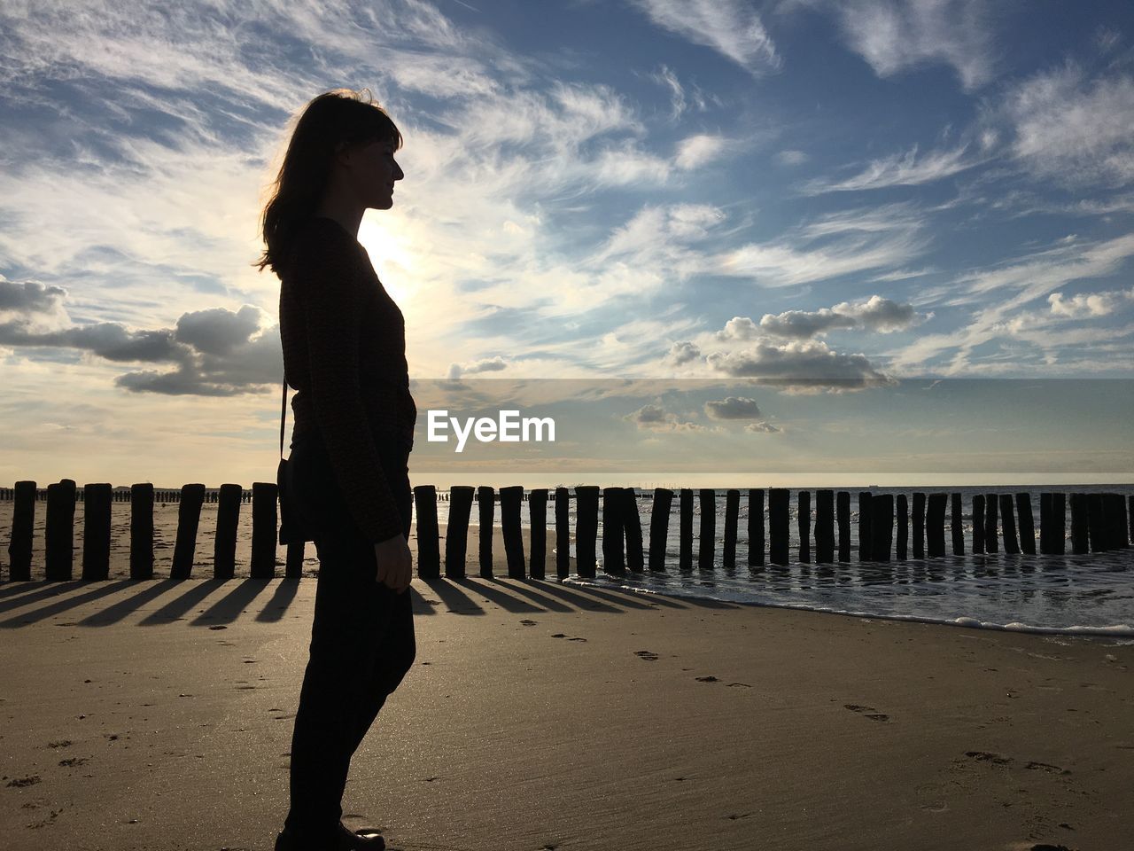 Silhouette of woman standing at beach against cloudy sky