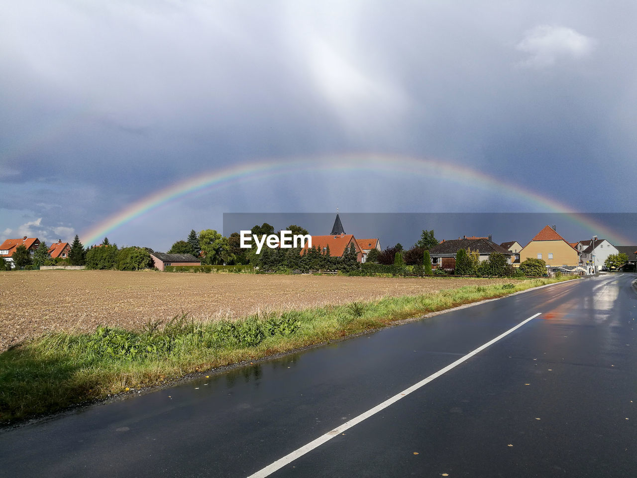 Rainbow over road amidst field against sky