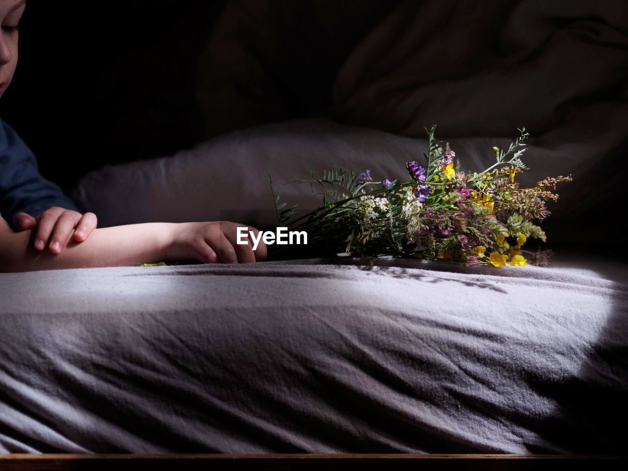 Cropped hand of child holding flowers on bed
