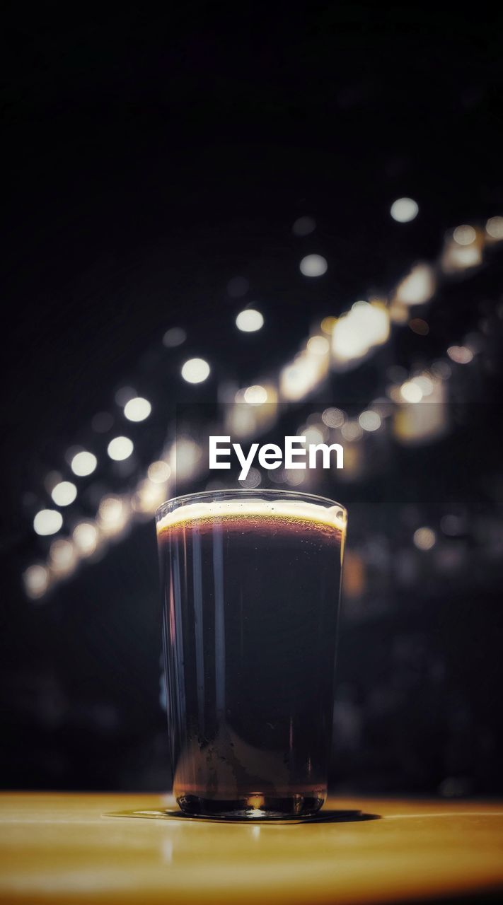 Close-up of dark beer in glass on table with blurred bar lights in the background