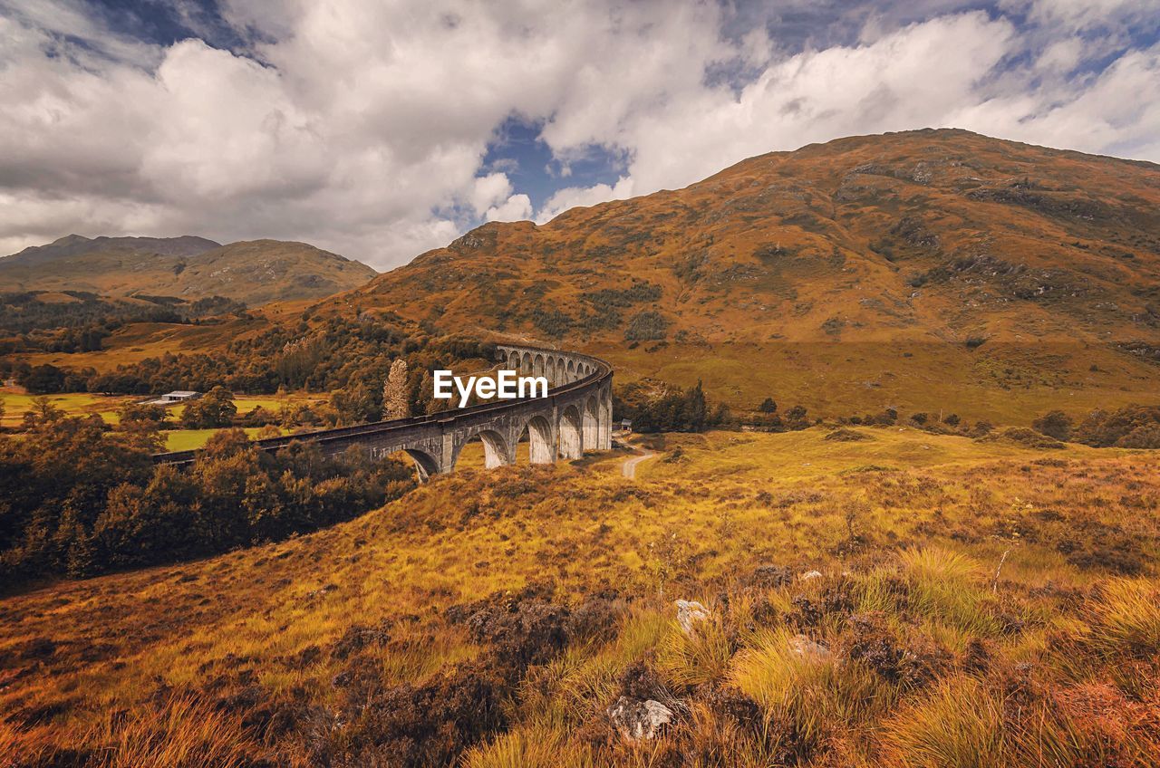 Bridge over field against cloudy sky at glenfinnan