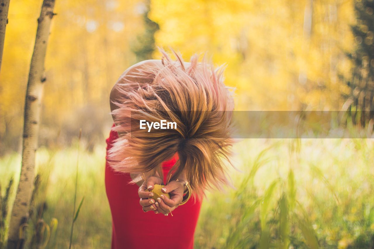 Woman with blond hair holding leaves while bending at forest